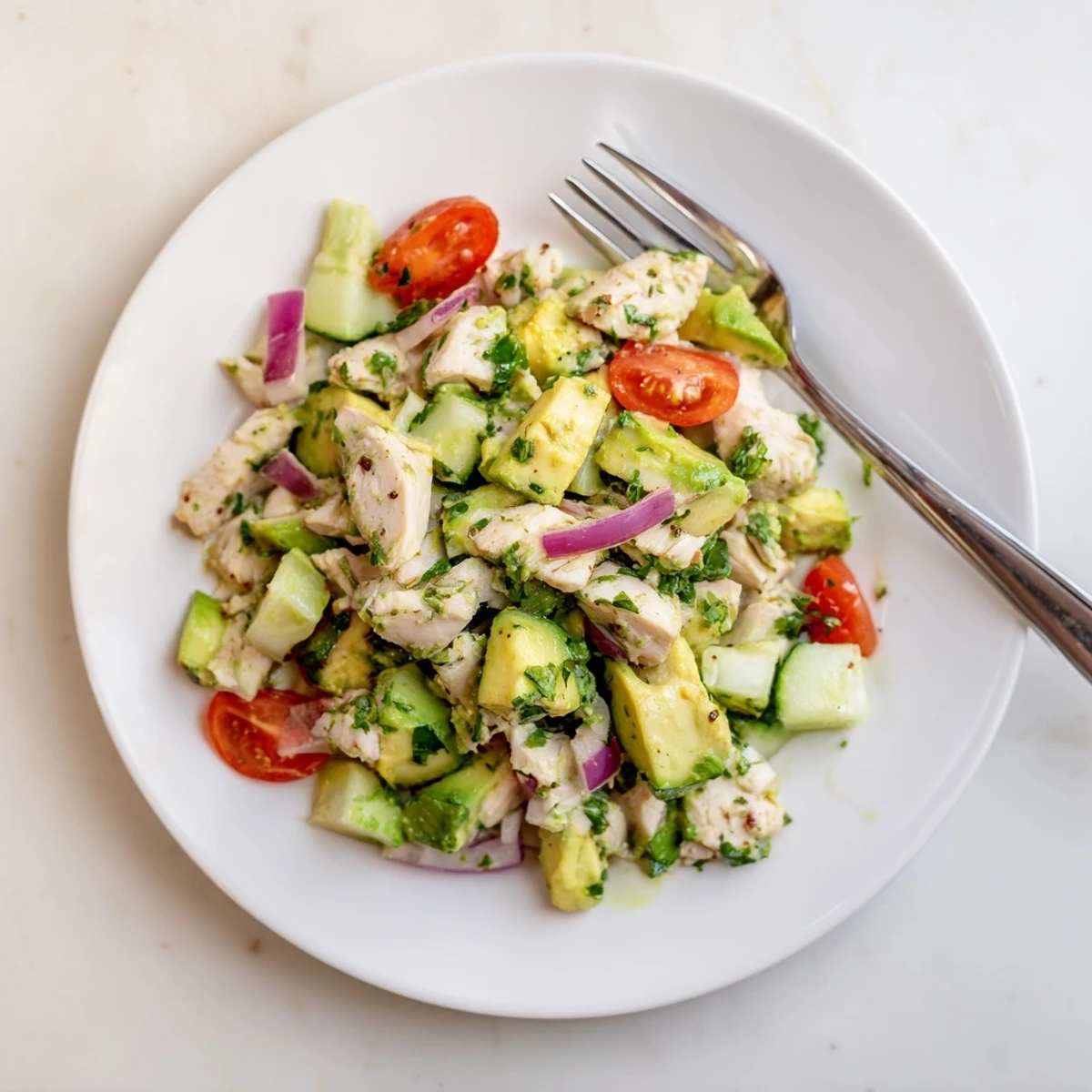 Creamy avocado chicken salad with tender chicken and bright lime, garnished with fresh cilantro in a white bowl.