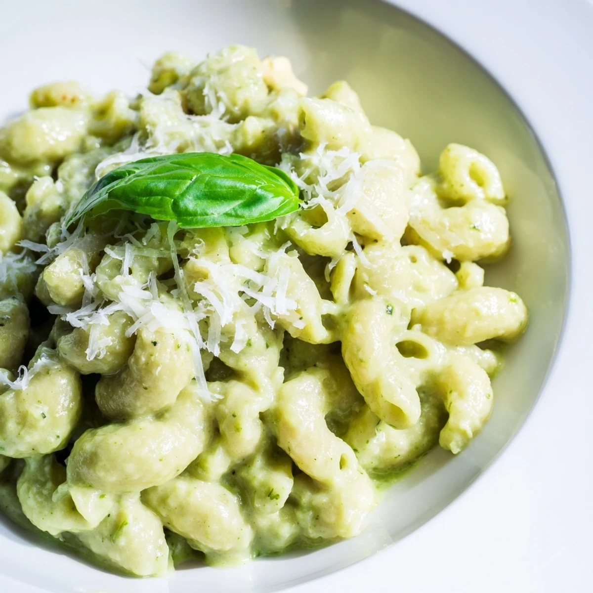 Fresh basil leaves and cracked pepper top a warm serving of Creamy Avocado Pesto Mac, ready to be enjoyed immediately.