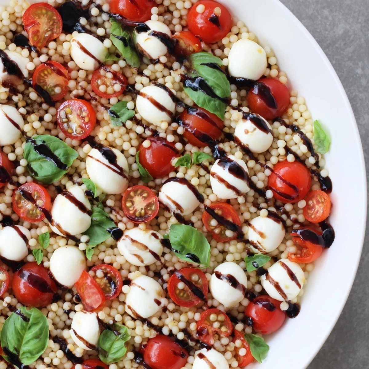 A close-up of Caprese Couscous Salad featuring tender pearled couscous, fresh basil, and a glistening balsamic glaze. 