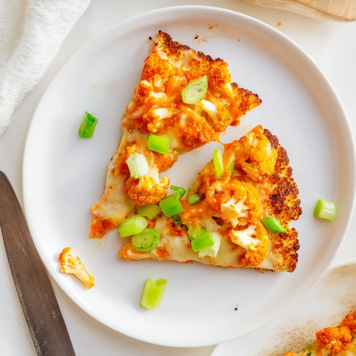 A vegetarian Buffalo Cauliflower Pizza topped with crumbled blue cheese and celery slices, sliced into generous wedges.  