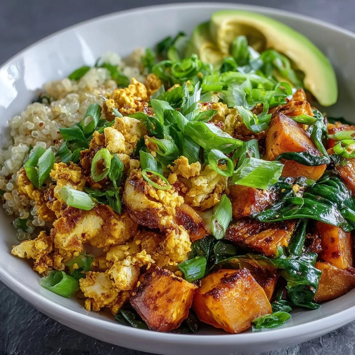 Vibrant vegan breakfast bowl with savory tofu scramble, roasted sweet potatoes, sautéed spinach, fluffy quinoa, and creamy avocado slices.  