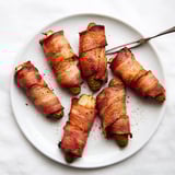 Twelve golden-brown bacon-wrapped pickle halves on a rustic platter, ideal for game day snacking.