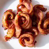 Golden-brown spiced bacon twists paired with fresh fruit on a wooden board for a festive snack.  