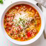 Cozy ladle of savory pizza soup topped with melted cheese and fresh basil garnish.  