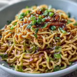 Aromatic Asian ginger scallion noodles with sautéed greens, glistening in savory sauce and topped with sesame seeds.  