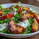 A summery grilled peach and burrata salad drizzled with honey and balsamic glaze, served on a bed of arugula.  