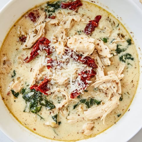 Creamy Tuscan Chicken Soup simmering in a pot with shredded chicken, wilted spinach, and vibrant sun-dried tomatoes in a herb-infused broth.