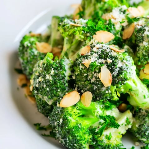 Bright green broccoli florets mixed with red onion, cherry tomatoes, and creamy Garlic Parmesan Broccoli Salad in a white bowl.