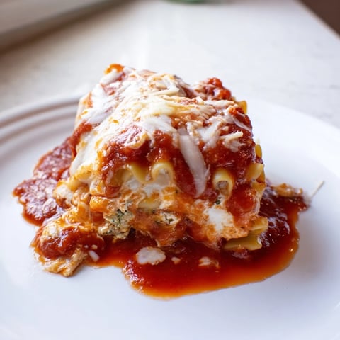 Golden-baked Chicken and Spinach Lasagna Rolls in a white baking dish, topped with bubbly marinara and melted mozzarella, garnished with fresh parsley.