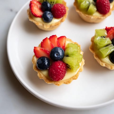 A close-up of beautifully arranged Mini Fruit Tartlets, piled high with fresh fruit and creamy filling.