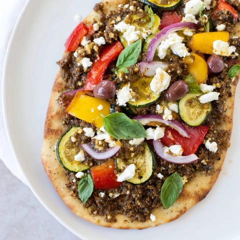 Crispy naan bread pizza features Mediterranean flavors: olive tapenade, feta, and sweet roasted veggies.