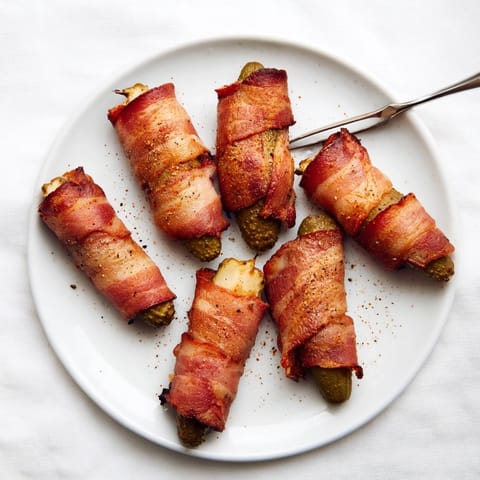 Twelve golden-brown bacon-wrapped pickle halves on a rustic platter, ideal for game day snacking.