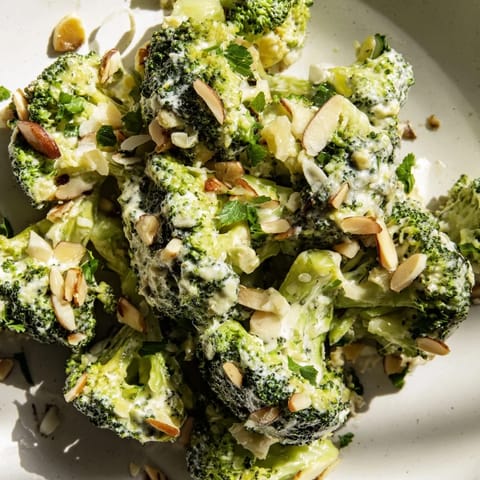 A fresh bowl of Garlic Parmesan Broccoli Salad garnished with toasted almonds, extra Parmesan, and parsley on a rustic table.