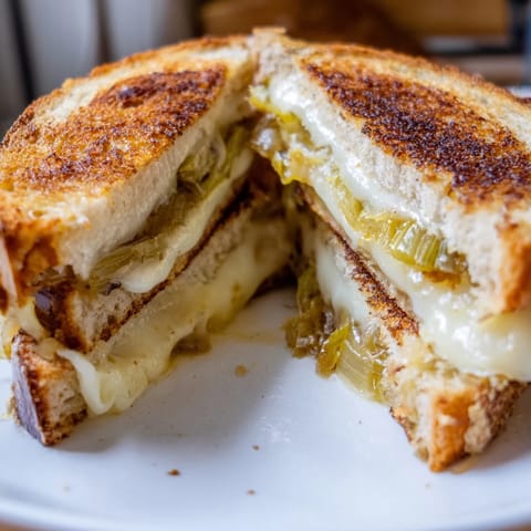 A close-up view of the Havarti & Caramelized Leek Grilled Cheese, with gooey cheese stretching from between crispy, golden-brown bread slices.