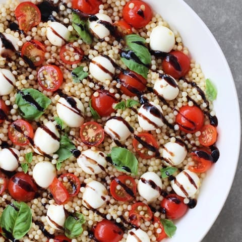 A close-up of Caprese Couscous Salad featuring tender pearled couscous, fresh basil, and a glistening balsamic glaze. 