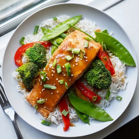 Glossy, caramelized Maple Soy Glazed Salmon resting on a fluffy bed of rice alongside vibrant, crunchy vegetables, with fresh lime wedges for a zesty finishing touch.