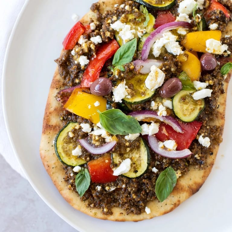 Crispy naan bread pizza features Mediterranean flavors: olive tapenade, feta, and sweet roasted veggies.