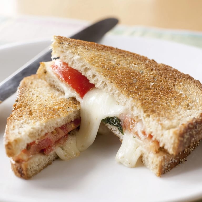 A crispy, golden Tomato Basil Grilled Cheese paired with ripe tomatoes and basil, ready to serve.