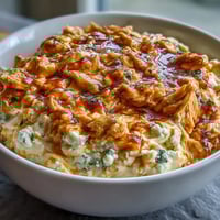 Creamy cottage cheese buffalo chicken dip with shredded chicken and spicy hot sauce, served bubbling hot in a baking dish with crisp celery sticks.